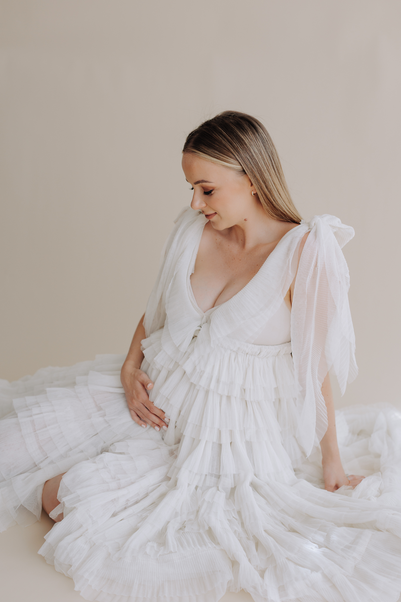 Blonde pregnant woman wearing a neutral marlize meeding dress in studio.