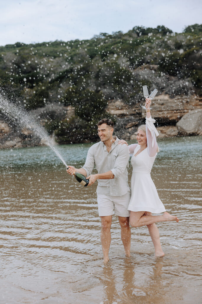 couple popping champagne on the beach